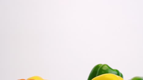 Colorful-medley-of-red,-orange,-yellow-and-green-bell-peppers-raining-down-and-bouncing-off-each-other-on-white-backdrop-in-slow-motion