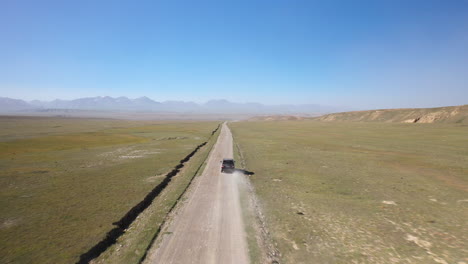 Tracking-drone-shot-of-a-vehicle-on-a-dirt-road-driving-near-Kel-Suu-lake-in-Kyrgyzstan