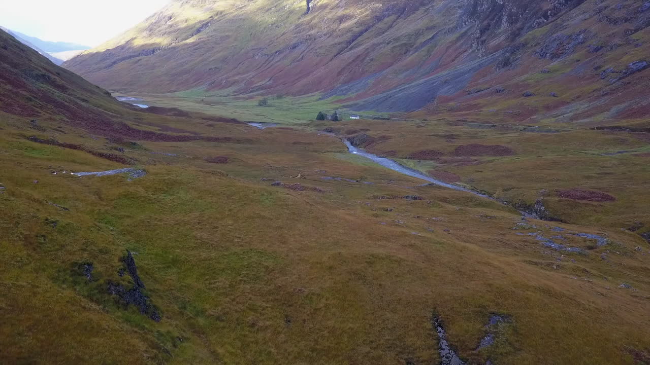 Ripresa aerea che sale sopra la cima di una collina per rivelare una remota valle fluviale in Scozia.