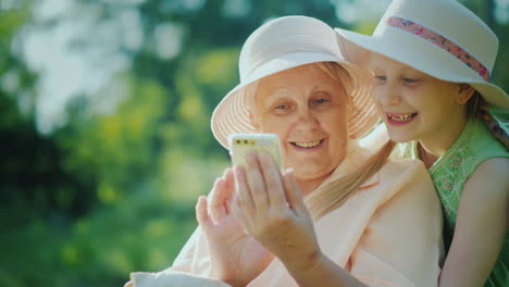 happy girl with grandmother looking at the smartphone screen together have a rest together in a summ