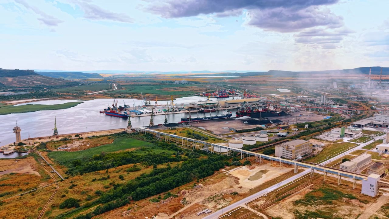 Varna, Bulgaria, 3 giugno 2026: Ponte trasportatore industriale che attraversa un paesaggio costiero verde. La struttura elevata si estende attraverso i campi verso un porto distante con navi da carico sotto un cielo nuvoloso.