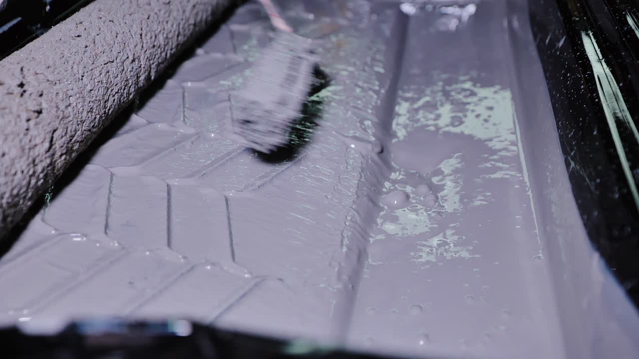 Macro shot showing paint roller absorbing gray paint in plastic tray indoors