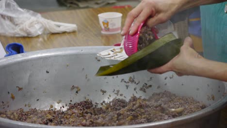 bowl of hot purple rice mixture placed into leaf wrap and hand folded by person