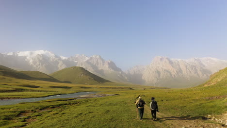 dos excursionistas en el sendero en el valle con la cordillera de kakshaal también en la distancia, kirguistán, avión no tripulado vuela más allá de dos hombres