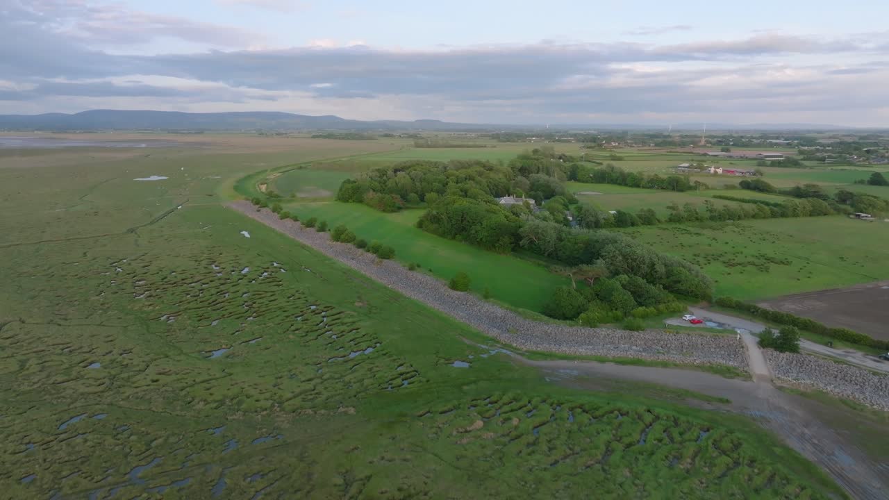 Tidal grassland giving way to arable farmland fields with mountains in the distance. Camera rise revealing landscape. Pilling Sands, Lancashire, UK.