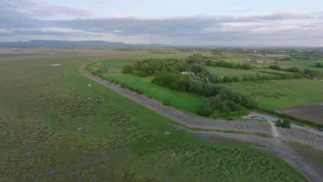 tidal grassland giving way to arable farmland fields with mountains in the distance. camera rise revealing landscape. pilling sands, lancashire, uk.