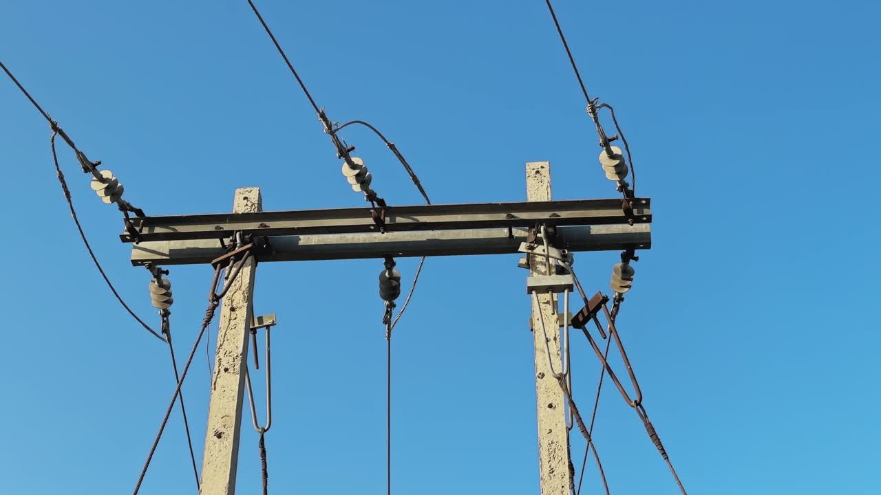 Static medium shot of a PSC or reinforced cement concrete power distribution pole in India, steel crossarm and ceramic insulators supporting low to medium voltage lines against a clear blue sky