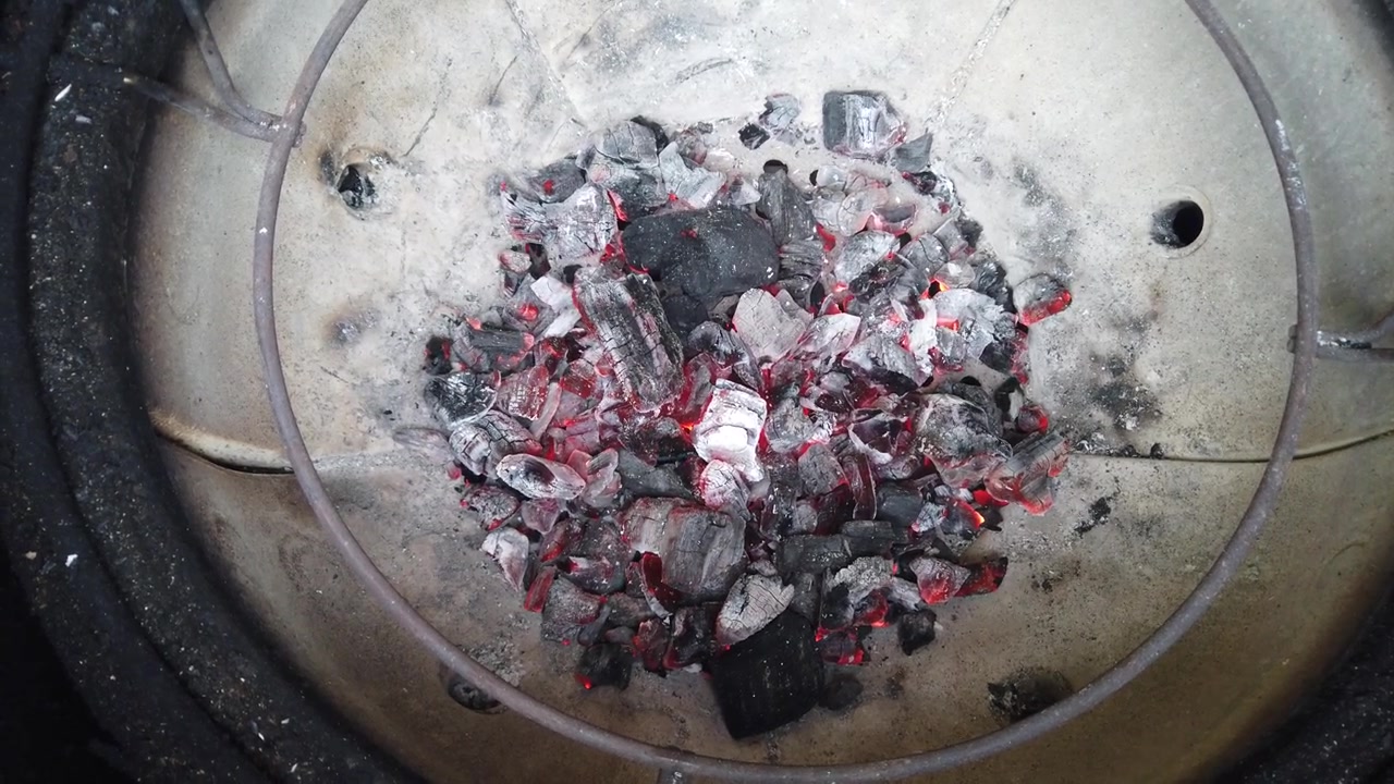 Pohled shora na žhnoucí a hořící horké dřevěné uhlíky uvnitř keramického grilu. Brikety doutnají a vytvářejí intenzivní teplo.