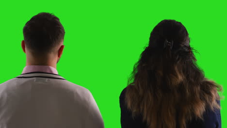 close up studio rear view shot of male and female teachers or businesspeople facing away from camera towards green screen