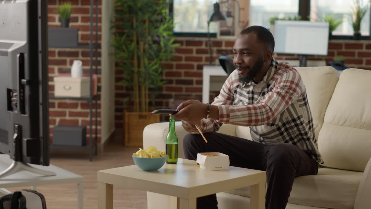 Male adult eating noodles with chopsticks at television