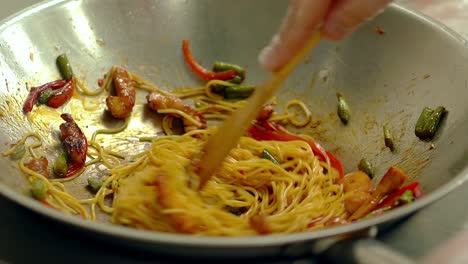 cu cocinero en cámara lenta prepara fideos pasta en una sartén en aceite con verduras frescas