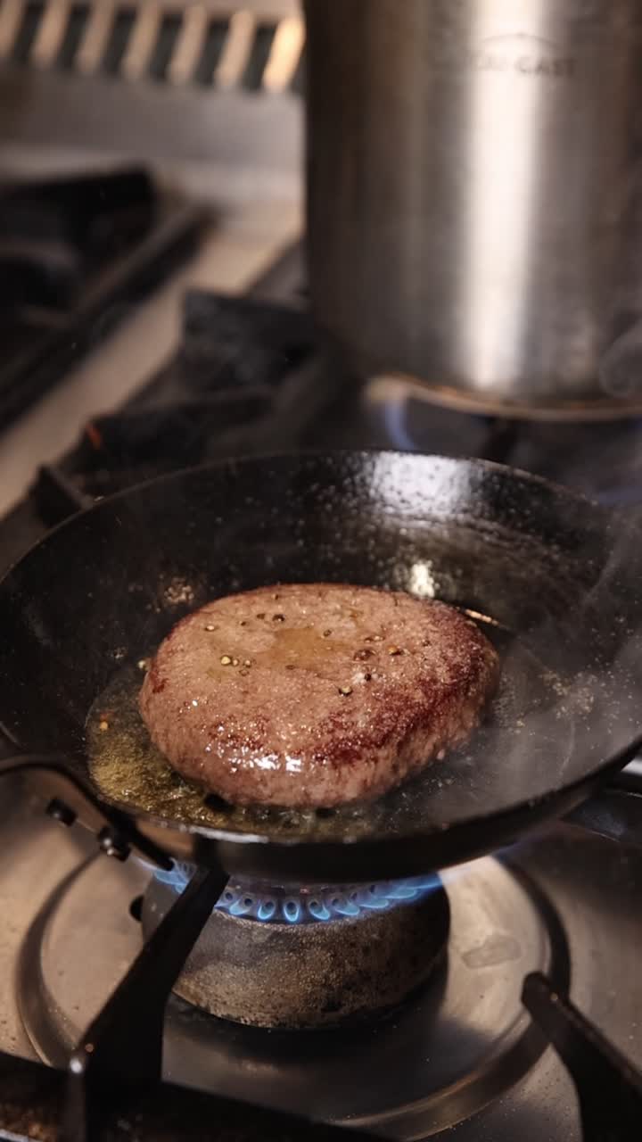En hamburgerbiff som steks i en het panna på en gasspis.