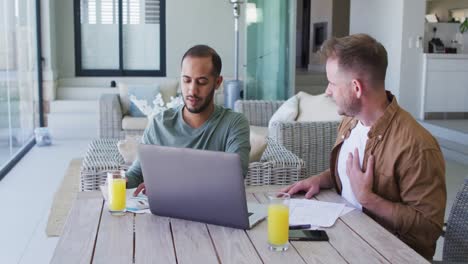 multi ethnic gay male couple sitting at table at homw using laptop