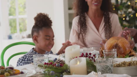 multi-generation family celebrating christmas at home saying prayer before eating meal together