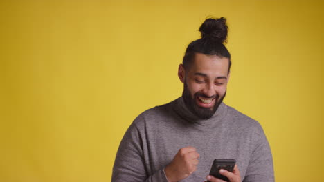 Studio Shot Of Smiling Young Man With Mobile Phone Getting Good News Against Yellow Background 1
