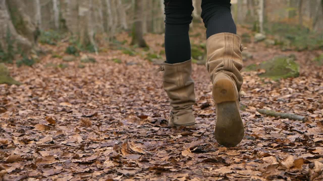 Woman in tall brown boots walks on autumn forest leaves, Slowmo with Copy Space