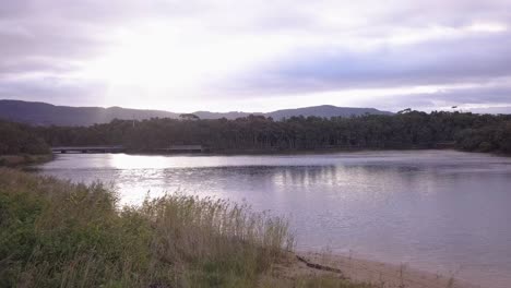 Flying-over-a-shiny-lake-surface-reflection-mirror-glassy-water-at-sunset