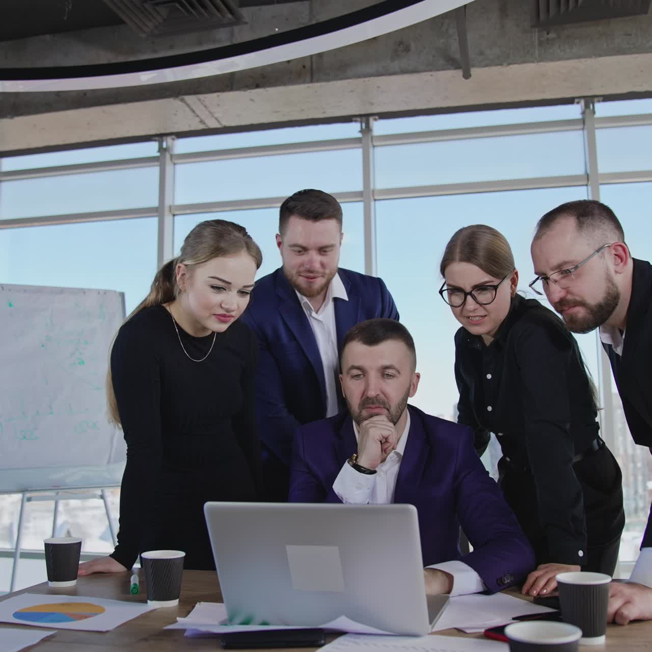 Teammates standing around the boss who's sitting in front of laptop. Brainstorming group collaborate and discuss something in computer