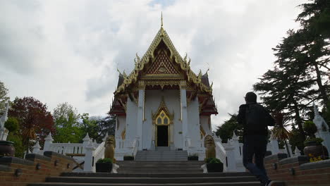 slow motion of a tourist man with a heavy backpack arriving at the hidden thai buddhist temple at sunset time and looking in the distance