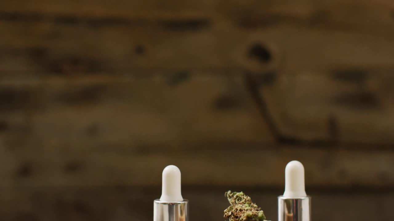 Ahşap arka plan üzerinde kenevir tomurcukları ve CBD özü şişeleri videosu