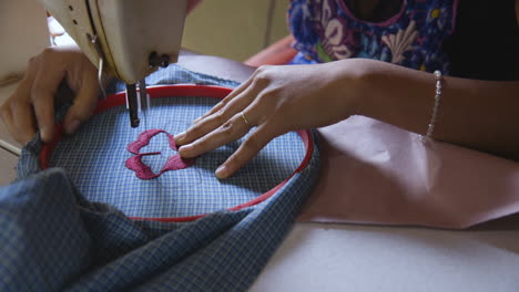 A-young-woman-using-a-sewing-machine-to-embroider-a-flower-on-a-traditional-apron-often-worn-in-San-Miguel-Del-Valle-in-Oaxaca,-Mexico