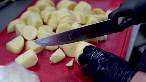 manos del chef particionando patatas crudas peladas en la tabla de corte roja, cerca