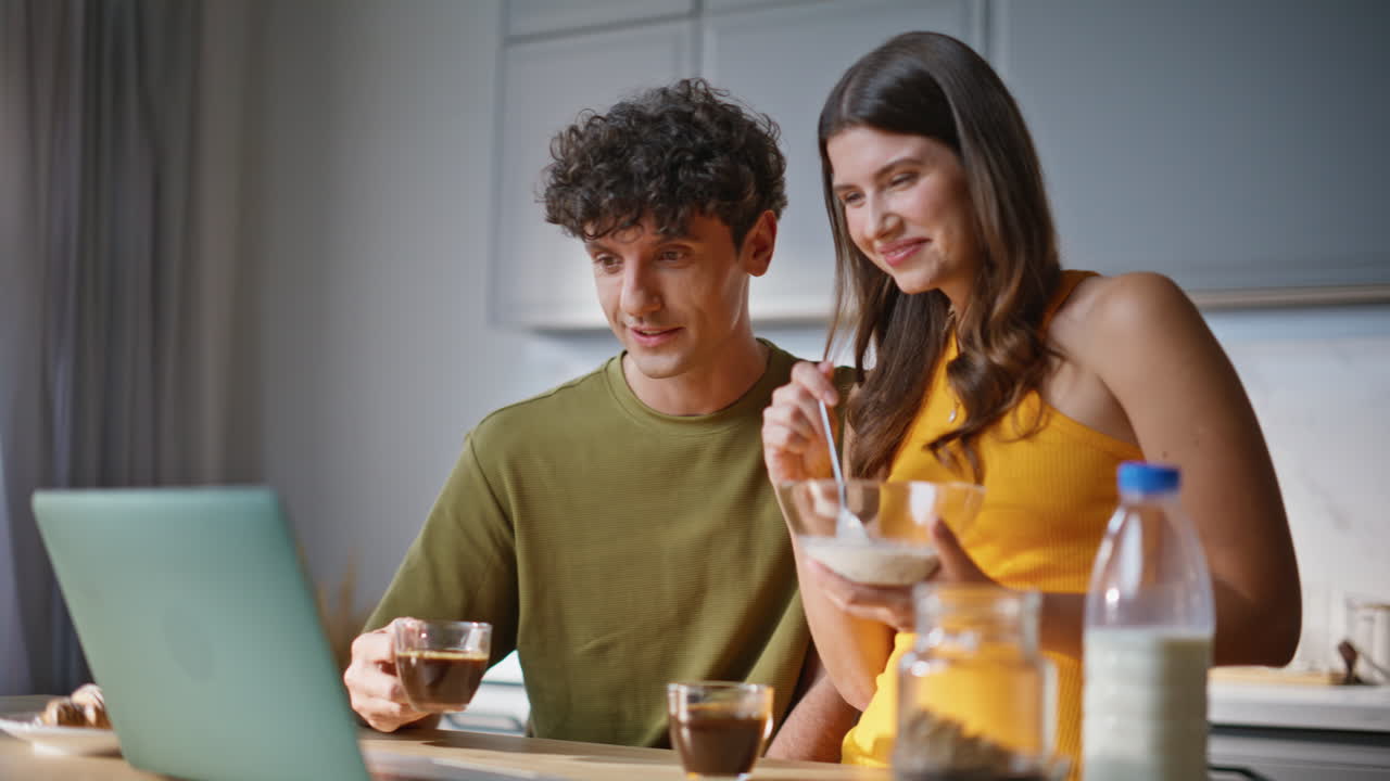 Home couple having breakfast at kitchen closeup. Lovers enjoying show at laptop