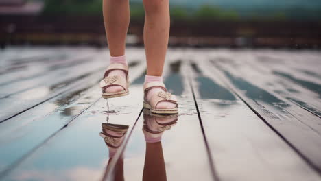 girl stamps feet in puddle of rain water on wooden deck