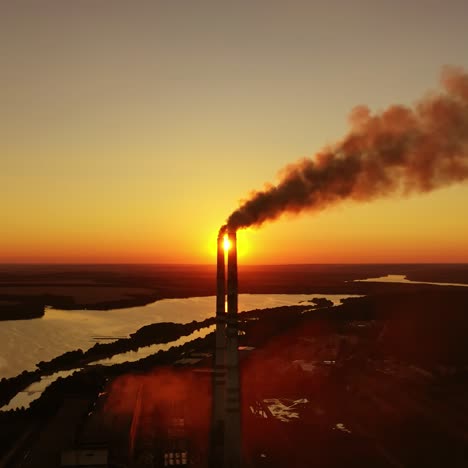 industrial pipes with thick smoke at dusk. chemical factory near the river against the orange sunset on the evening sky. ecological disaster. aerial view.