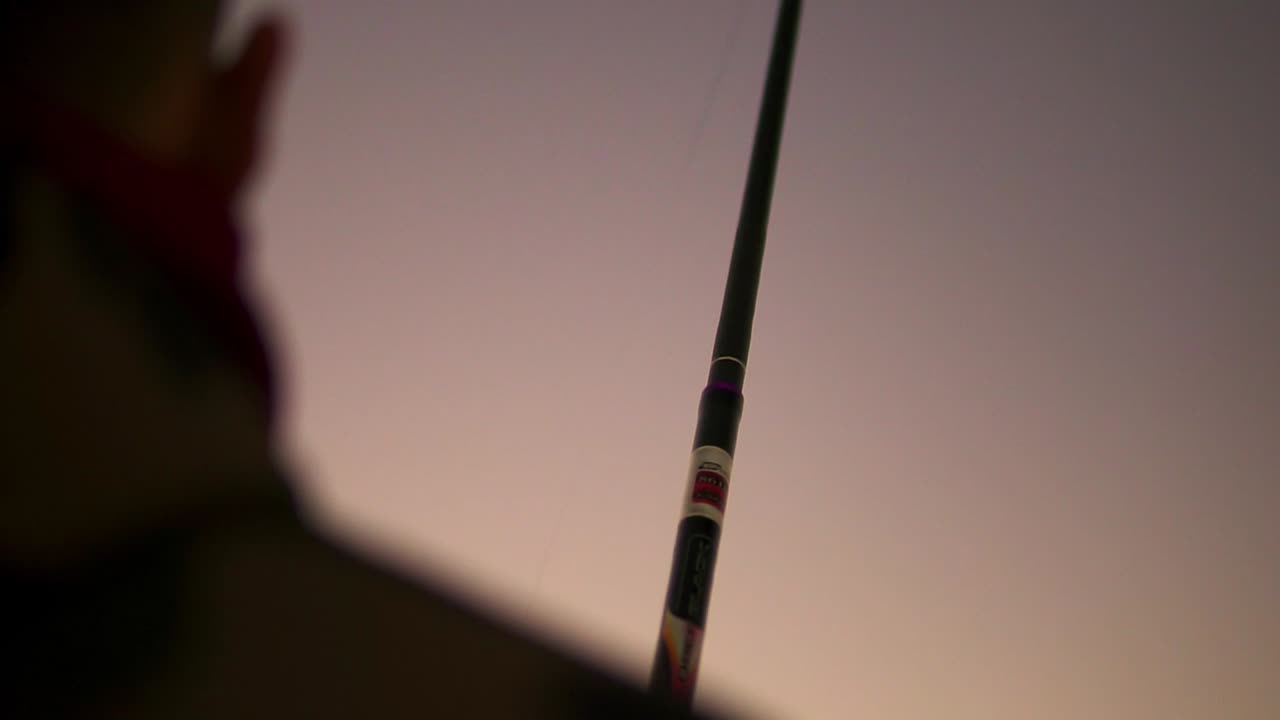 persona sosteniendo una caña de pescar en una puesta de sol naranja