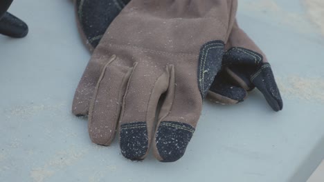 un par de guantes de construcción de carpintero de cuero marrón sobre una mesa gris cubierta de partículas de madera de aserrín en el lugar de trabajo activo