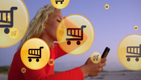 animación de iconos de compras sobre la sección media de una mujer caucásica usando un teléfono inteligente en la playa