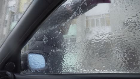 una mujer raspa el hielo del parabrisas de su coche después de un largo estacionamiento.