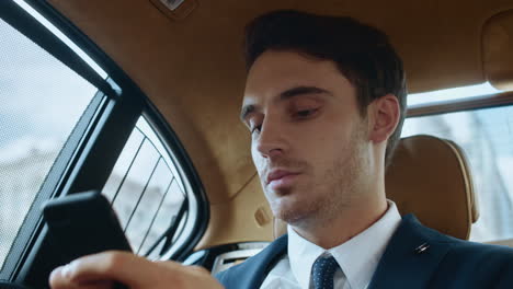 Portrait-of-focused-business-man-writing-message-on-phone-in-luxury-automobile.