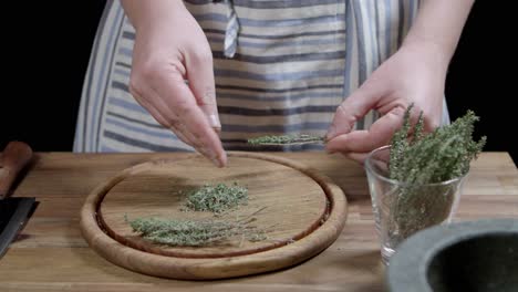 Chef-shreds-fresh-thyme,-with-his-fingers-on-a-wooden-board