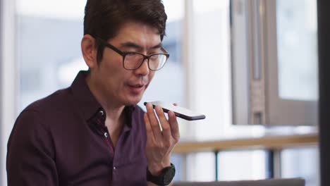 Asian-man-with-laptop-talking-on-smartphone-while-sitting-at-a-cafe