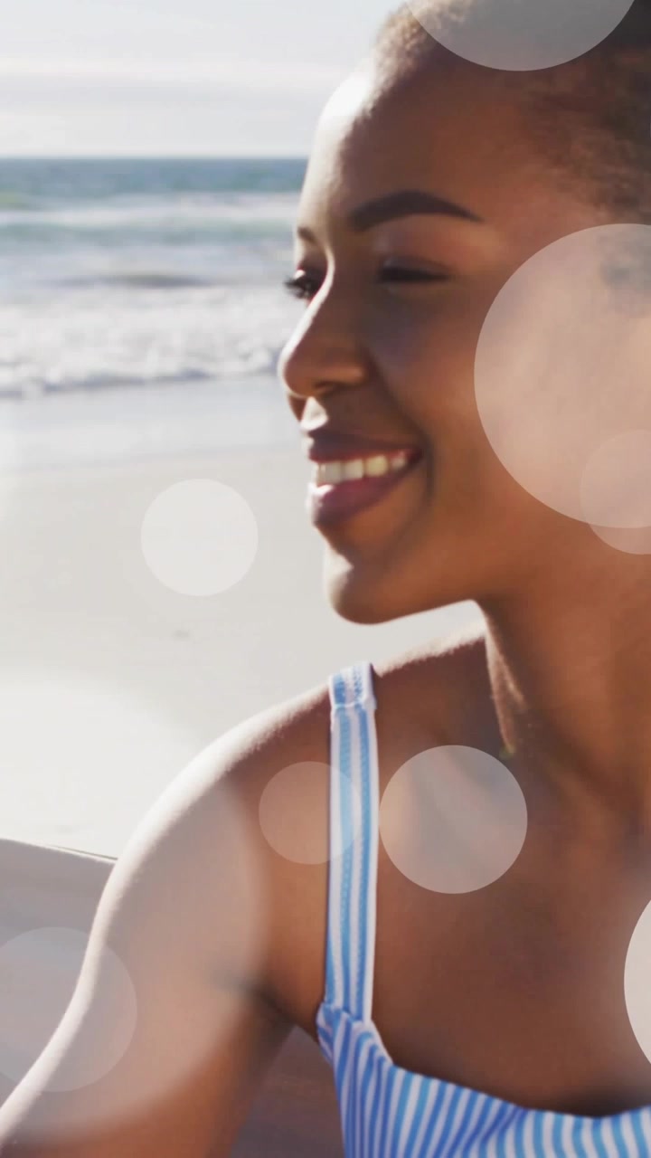 Vertical video: Woman sitting on beach cam zooming, smiling as bokeh crossing face aiding marketing