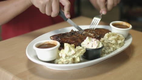 man slicing and eating pork ribs with mashed potato and vegetable salad side dish