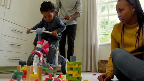 Vista-De-ángulo-Bajo-De-Un-Joven-Padre-Negro-Enseñando-A-Su-Hijo-A-Andar-En-Triciclo-En-Una-Casa-Cómoda-4k