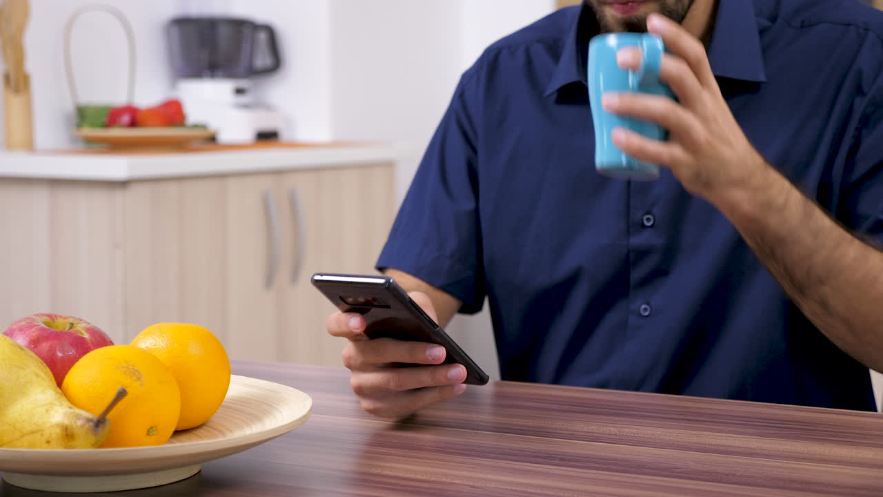 Man using mobile phone at kitchen table with fruits and cup