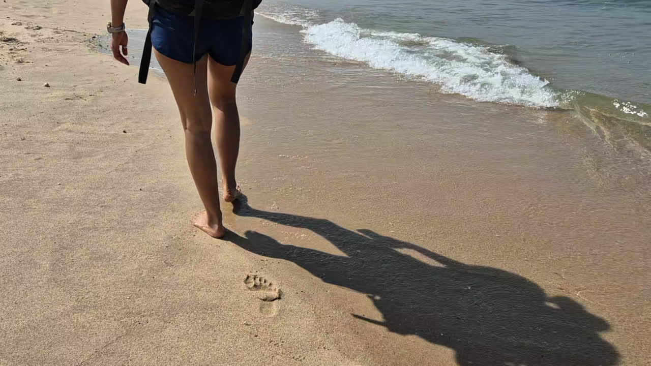 Barefoot female backpacker hikes on beach sand near gentle waves