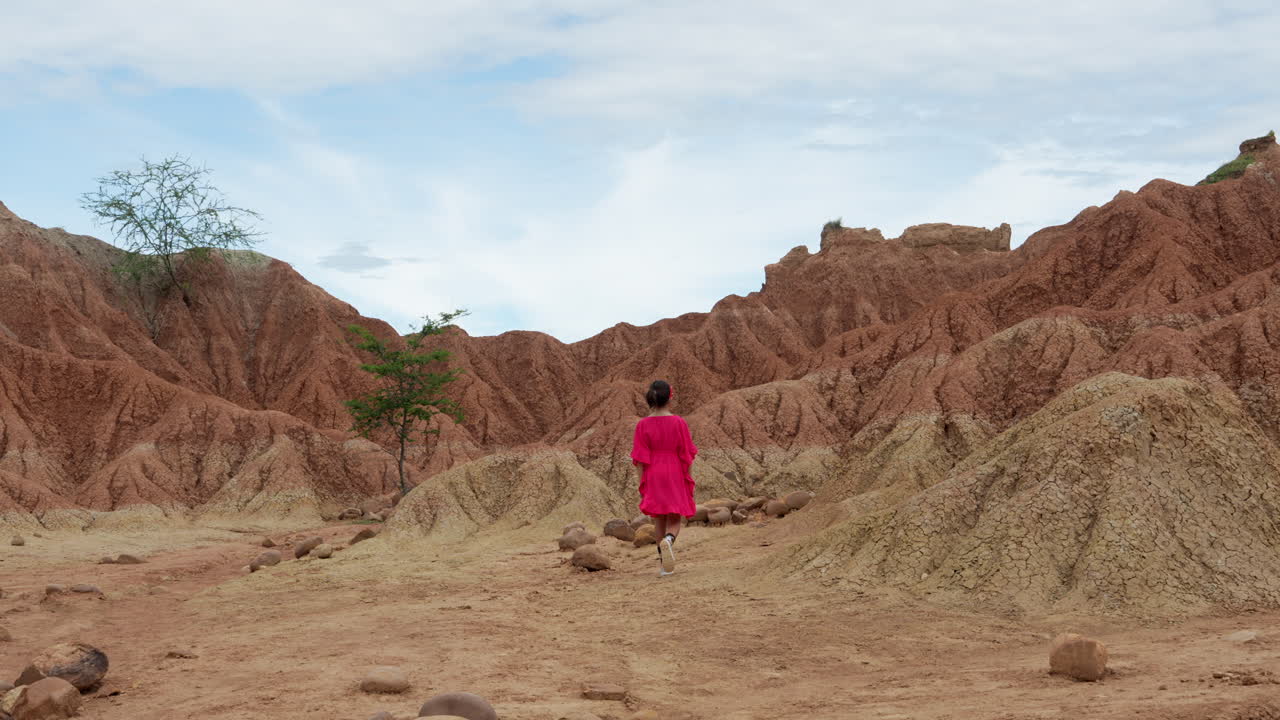 A young girl in vibrant attire explores the rugged, red terrain of Tatacoa Desert under a bright sky, capturing the essence of adventure and serenity in this expansive wilderness.