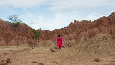 a young girl in vibrant attire explores the rugged, red terrain of tatacoa desert under a bright sky, capturing the essence of adventure and serenity in this expansive wilderness.