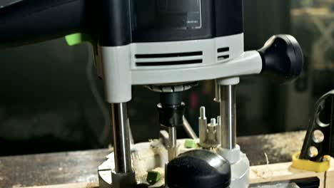 primer plano de la mano de un carpintero trabajando con un cortador eléctrico manual en un taller casero.