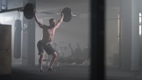 slow motion: brutal athlete lifts the bar above himself performing a jerk a spinning push. a man is engaged in weightlifting on a dark background portrait. concept strength power playing sports.