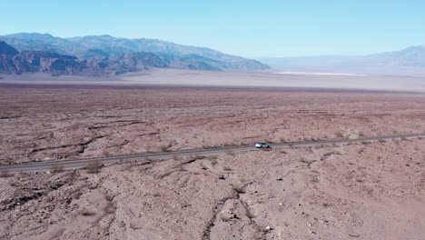 fotografía aérea cinematográfica de un coche tesla blanco moviéndose en medio del desierto de mojave