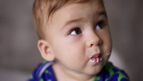 adorable innocent baby boy with grey eyes and smudged face eating dairy. feeding little child from spoon. close up.