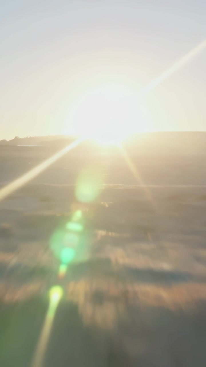 Vertical video: Rising sun hitting horizon, creating green flare orbs, streaks, ridge, blurred land