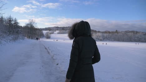 Young-woman-wearing-winter-gear-strolling-through-winter-wonderland-forest-with-snow-covered-firewood-during-winter-in-Bavaria,-Germany