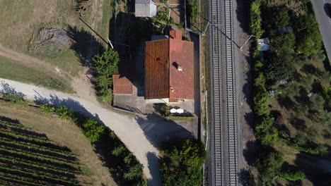 Vista-Aérea-De-La-Casa-Rural-Italiana-Junto-A-Las-Vías-Del-Tren-Y-Viñedos-Verdes-Campiña-Italiana,-Toscana